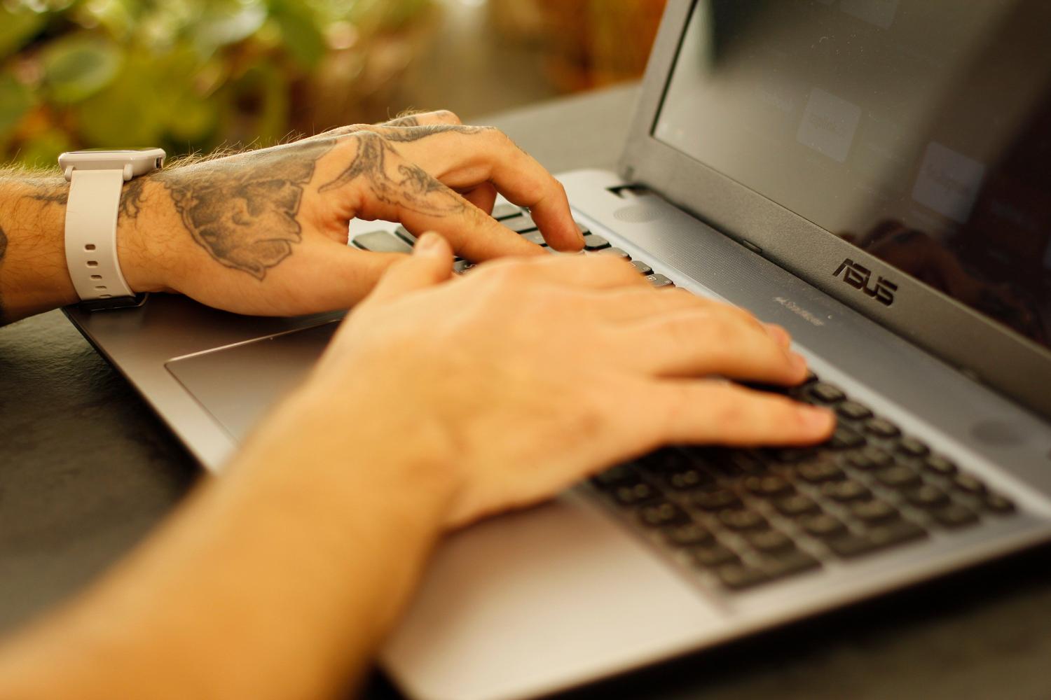 Primer plano de manos escribiendo en el teclado de una computadora portátil, enfocándose en la interacción con el software.