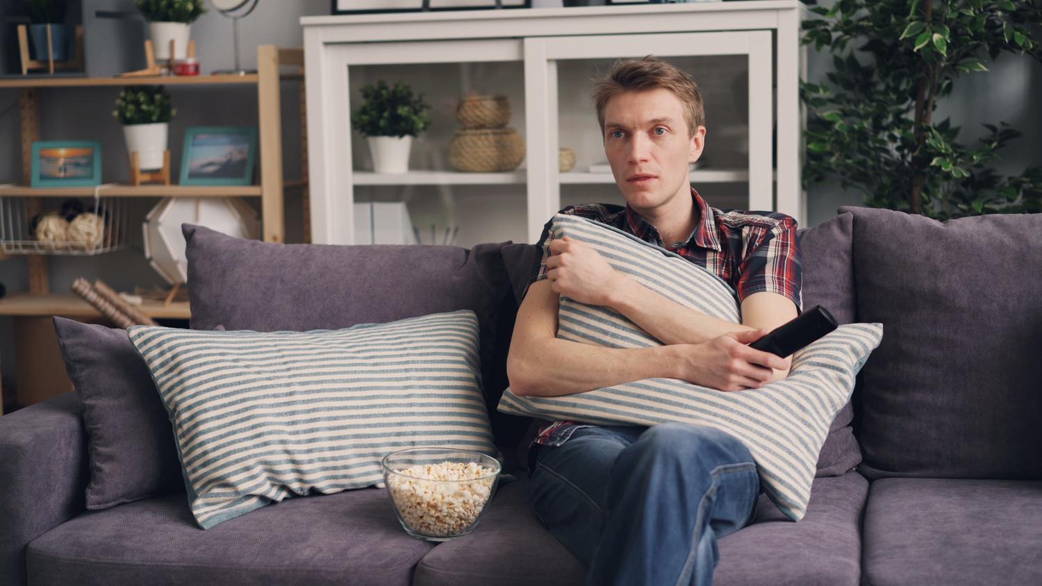 Un hombre joven disfrutando de un maratón de anime en la televisión con un bol de palomitas.