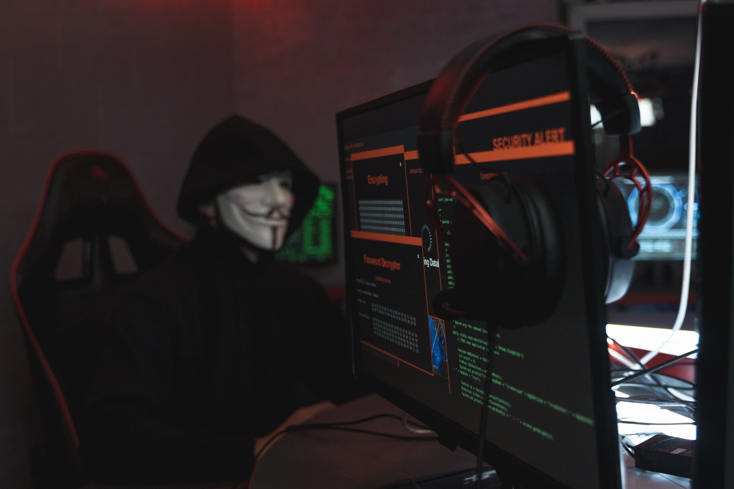 Persona encapuchada operando un ordenador en uma habitación oscura, simbolizando los riesgos de malware, troyanos y ciberataques que el software de seguridad previene.