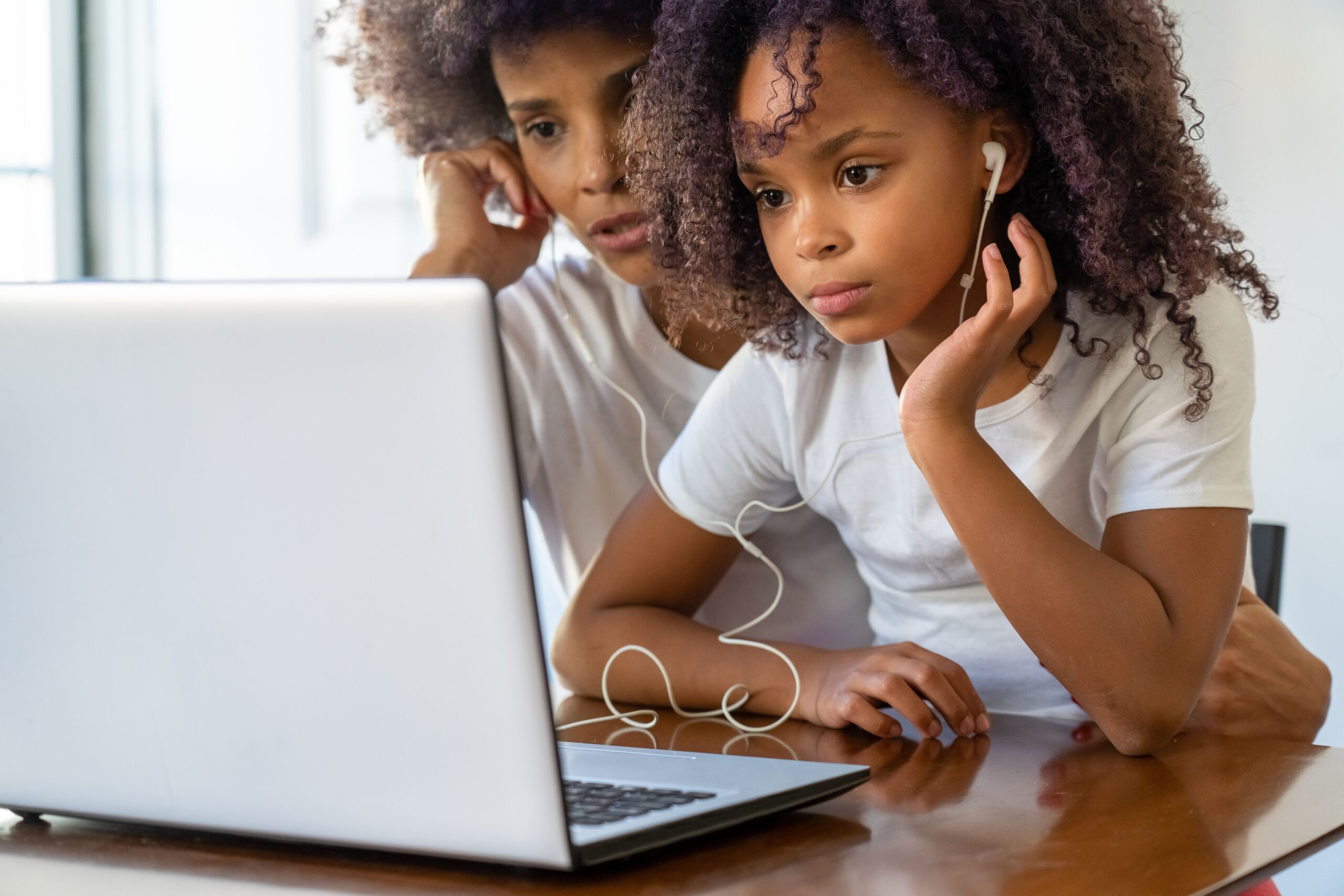 Uma mãe e sua filha utilizando juntas um computador portátil em casa, representando o uso supervisionado e o controle parental.