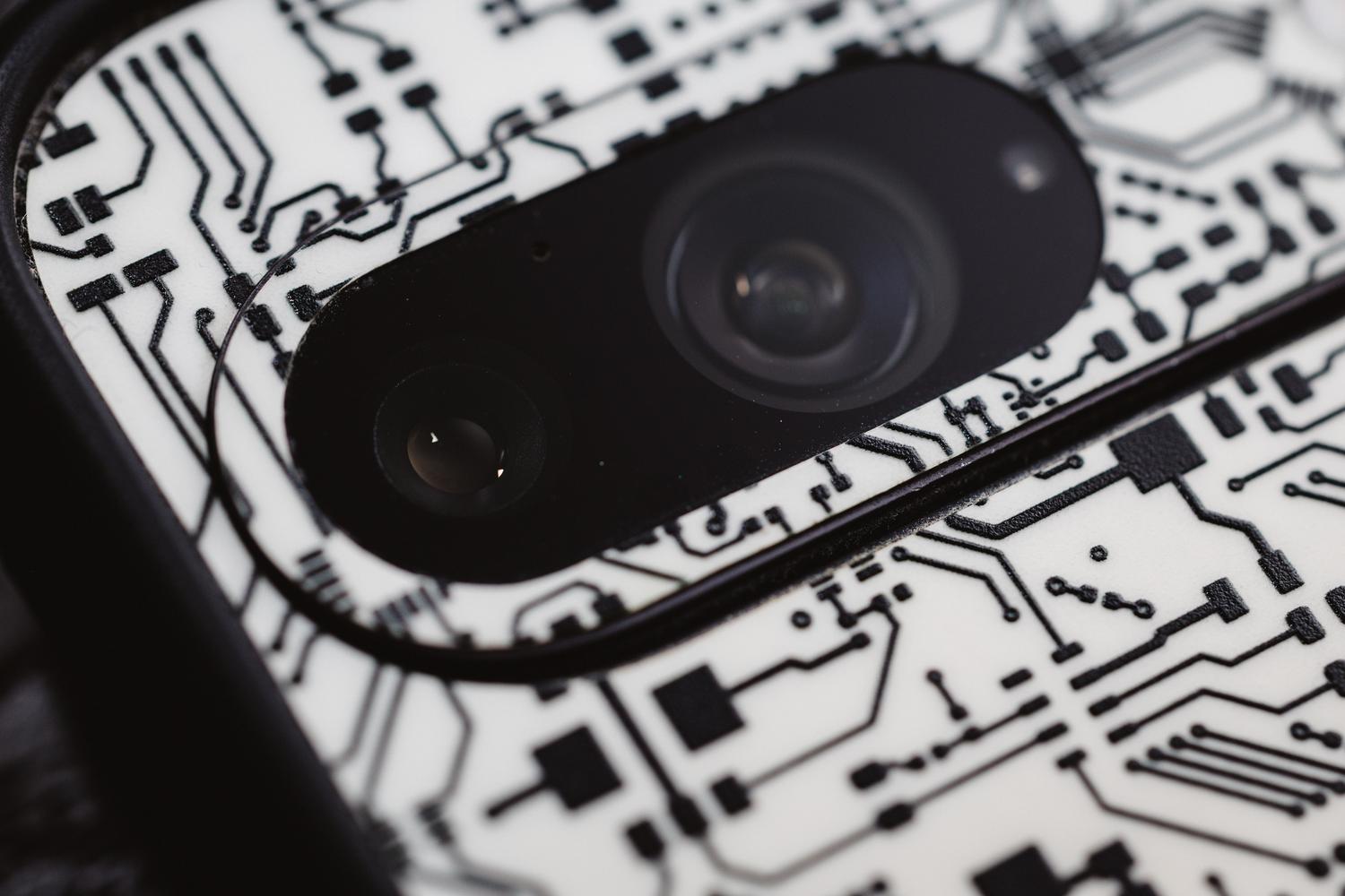 Detalle macro de um circuito electrónico junto a la lente de la cámara de um smartphone, representando la innovación y el I+D.