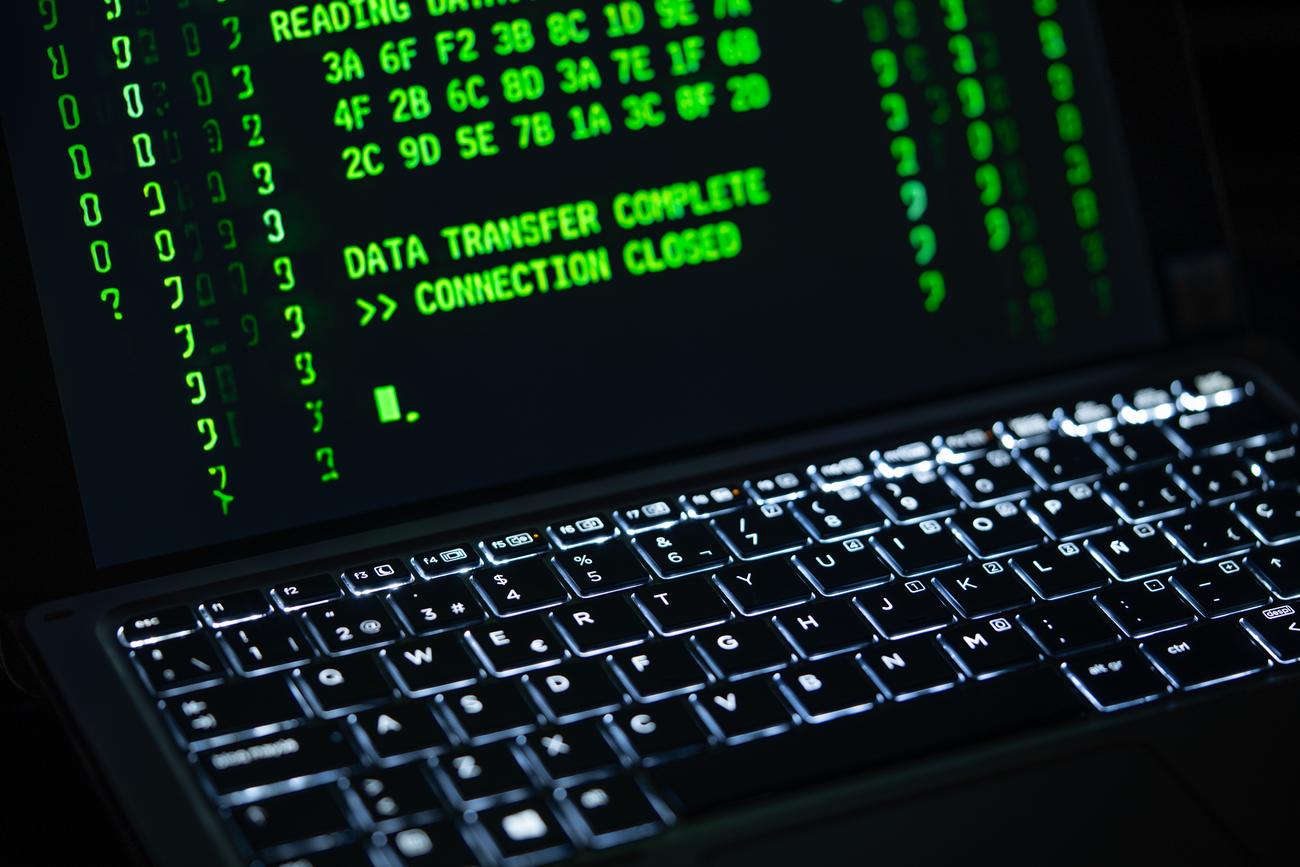 Close-up of a laptop screen with green digital code, representing the technical nature of malware and cybersecurity.