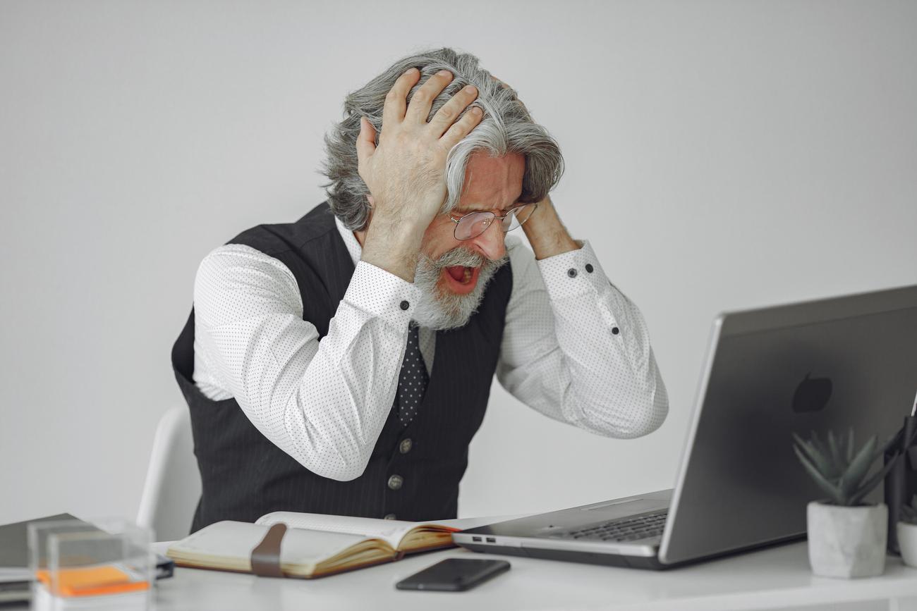 Frustrated man shouting at his laptop, illustrating the stress of dealing with software uninstallation errors.