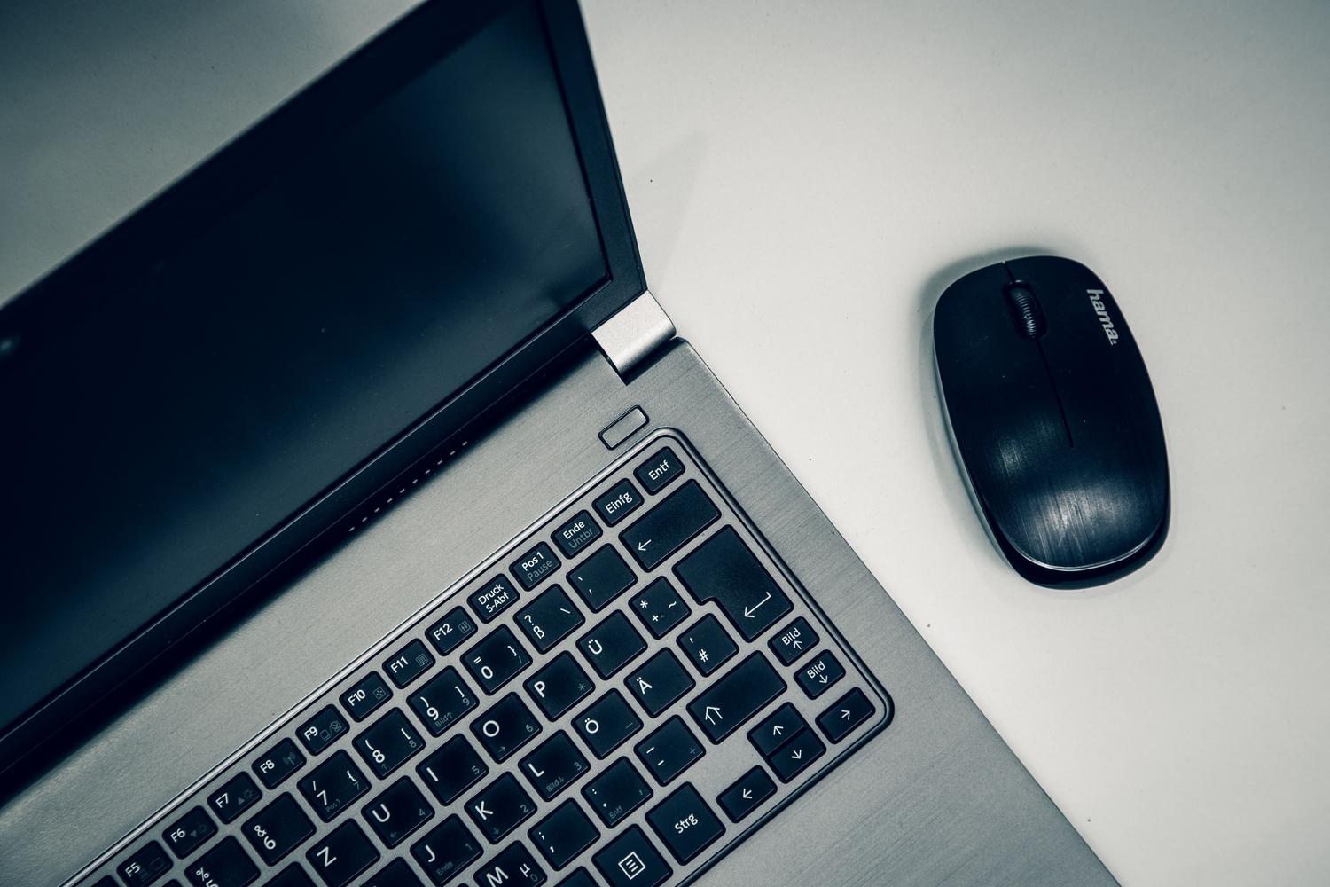 Portátil tradicional plateado con ratón inalámbrico sobre un escritorio blanco, representando la versatilidad y funcionalidad del laptop clásico.