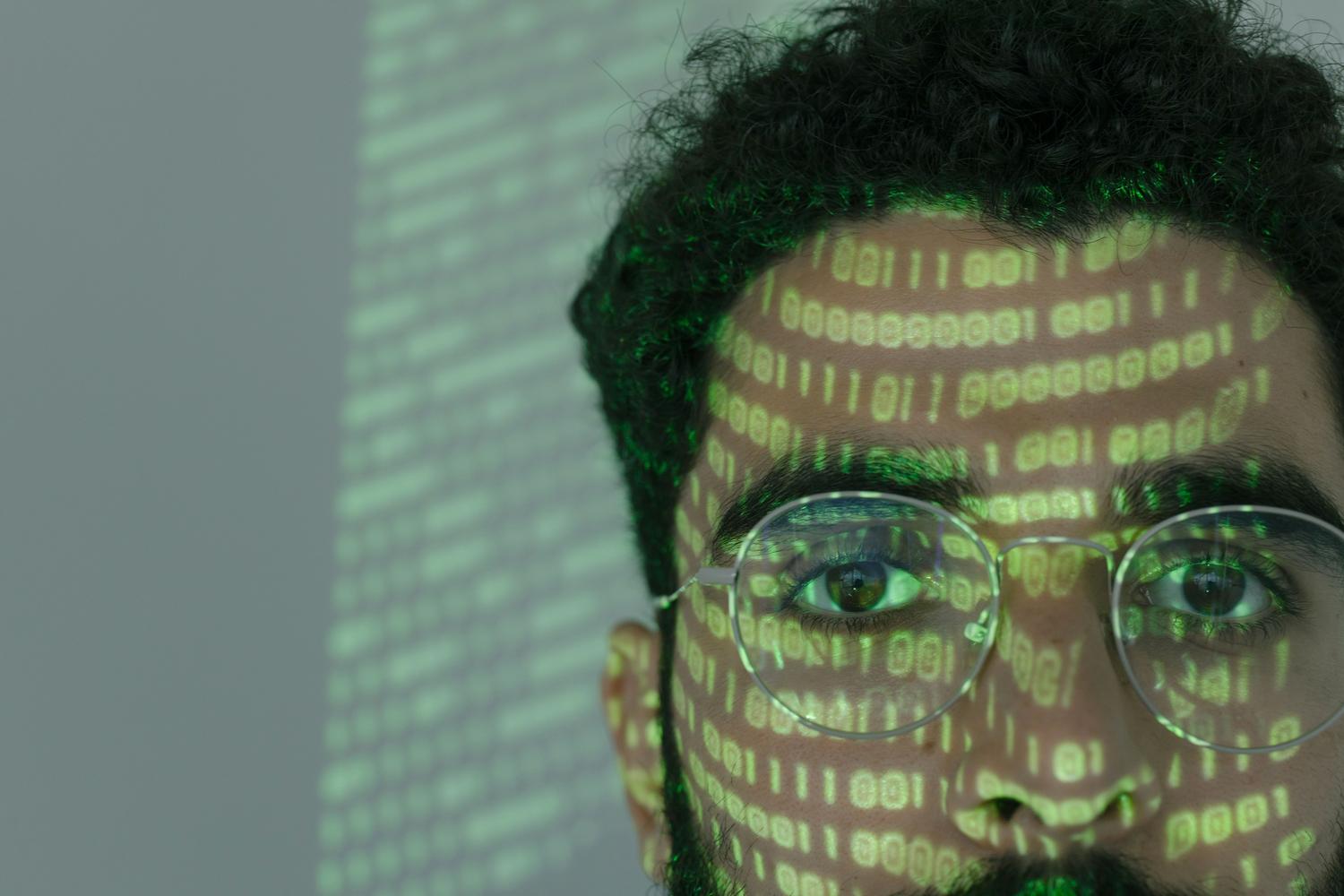 Primeiro plano de um homem com código binário projetado em seu rosto, representando o anonimato e o mistério da Dark Web.