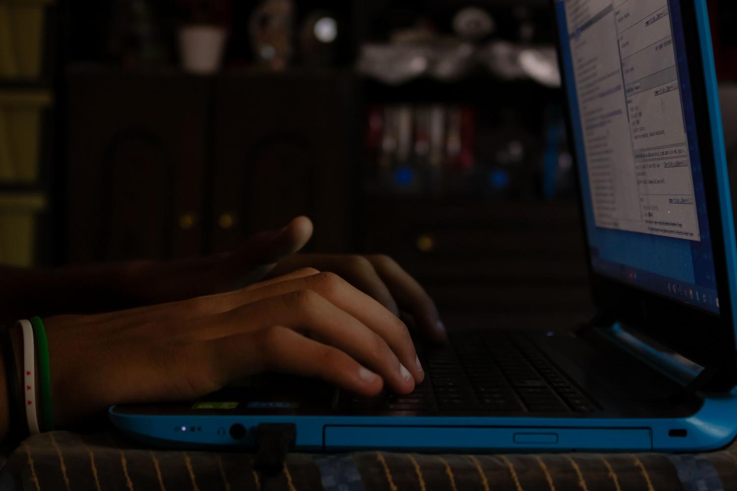Manos tecleando en un portátil en un entorno con poca luz, evocando la navegación por foros y comunidades online desde casa.