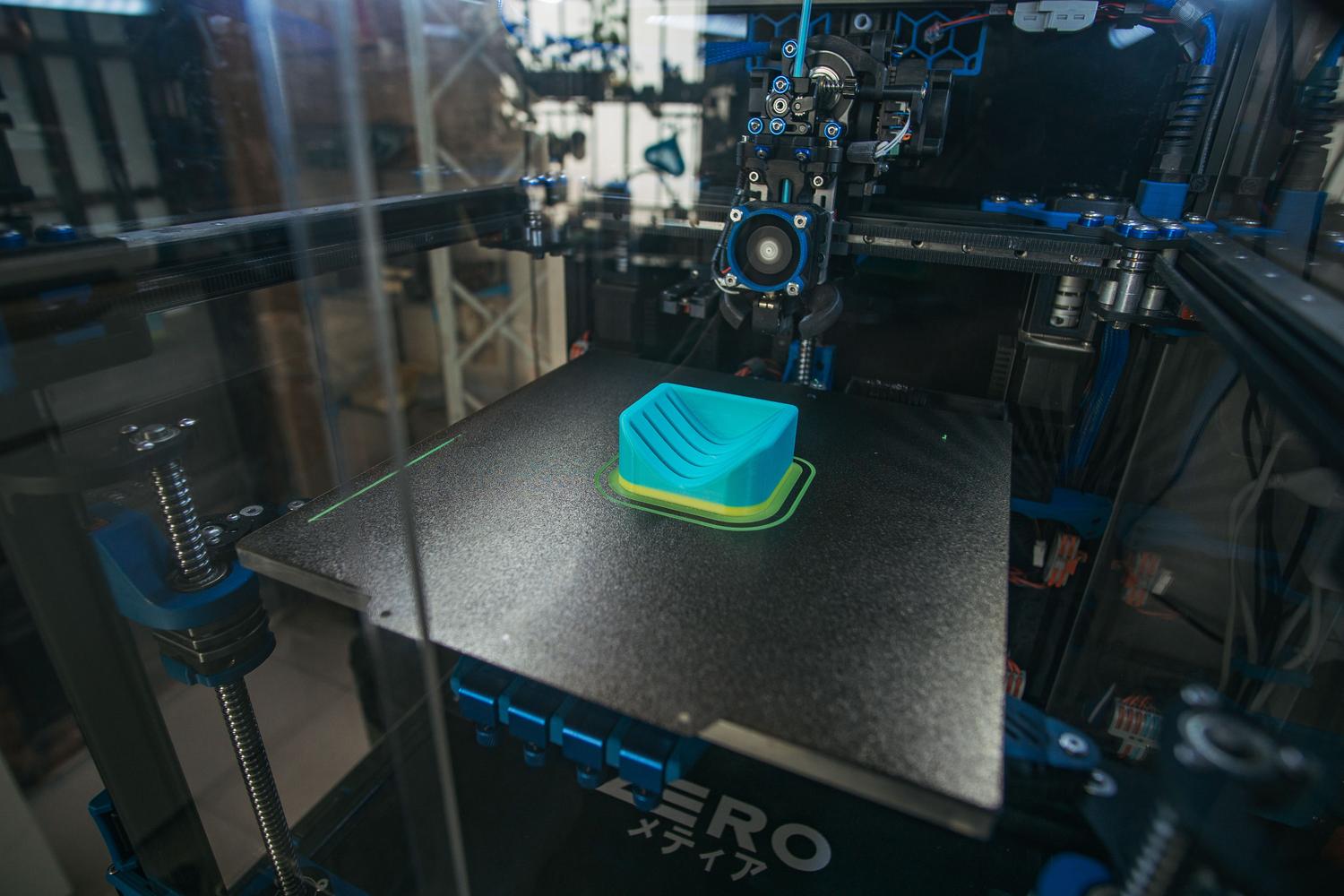 Primer plano de una impresora 3D en un entorno industrial, enfocada en la producción de prototipos.
