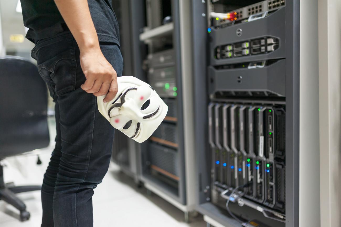 Máscara anónima junto a servidores de datos, simbolizando el mercado clandestino de la dark web y el Malware-as-a-Service.