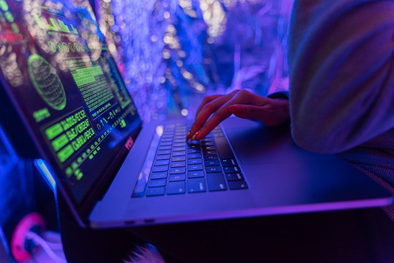 Primer plano de manos escribiendo en un teclado iluminado con luz púrpura, simbolizando la ejecución silenciosa de scripts maliciosos.
