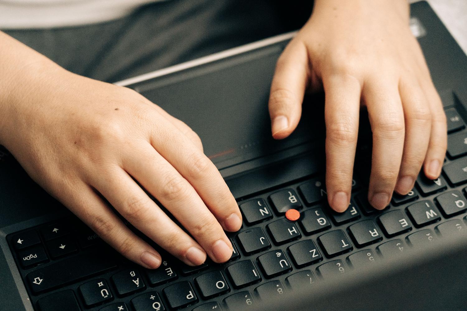 Primer plano de unas manos escribiendo en el teclado de un portátil, ilustrando el uso de atajos de teclado.