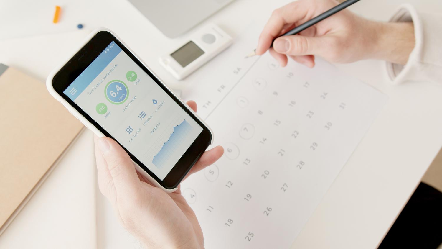 Primer plano de manos utilizando un smartphone para programar fechas en un calendario.