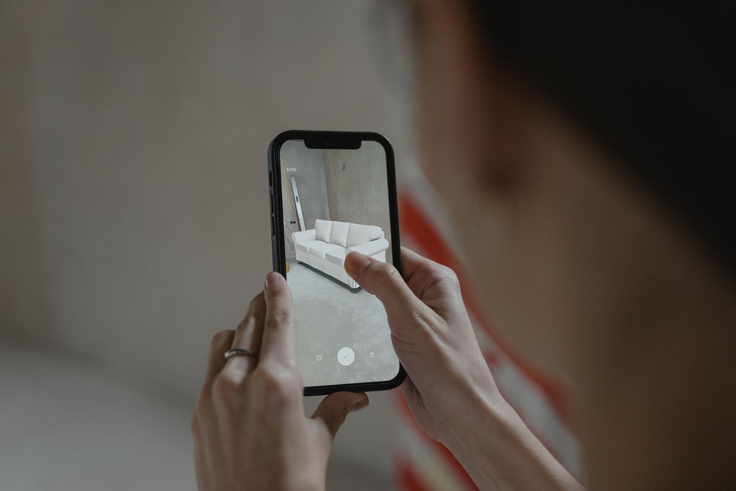 Persona utilizando realidad aumentada en un smartphone para visualizar un sofá en una habitación.
