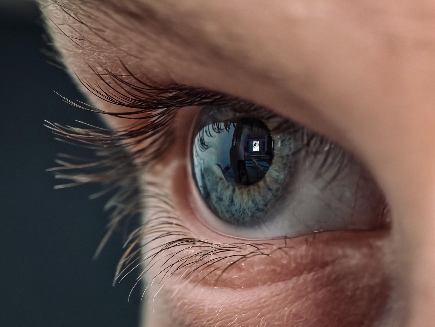 Primer plano macro de un ojo humano reflejando la luz de una pantalla digital, mostrando la causa principal de la astenopia digital.