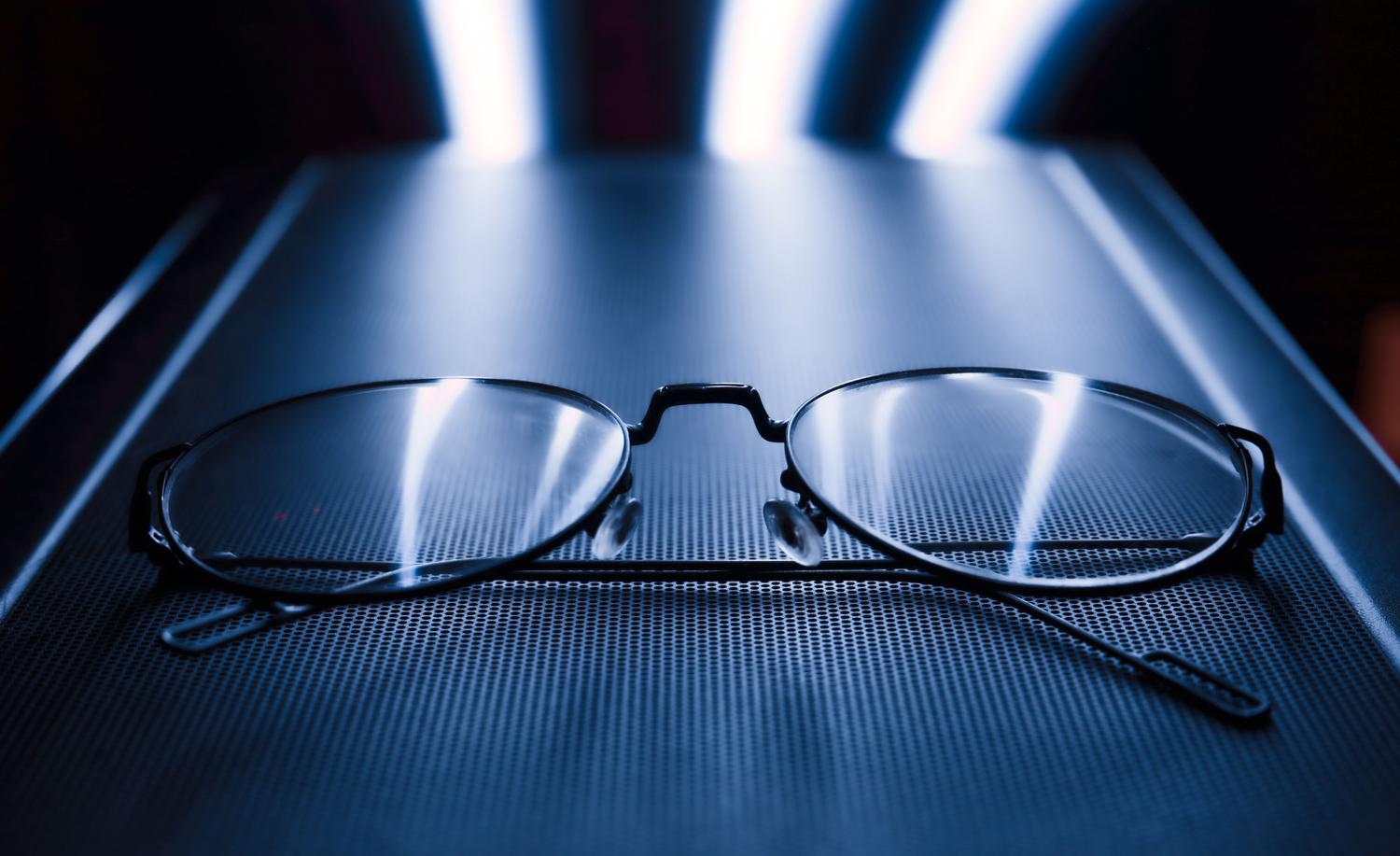 Gafas con reflejos azules sobre fondo tecnológico, representando las lentes con filtro de luz azul para proteger la vista.