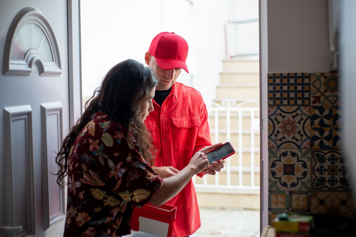 Mujer recibiendo un paquete de un repartidor en la puerta de su casa tras abrir el acceso desde el móvil