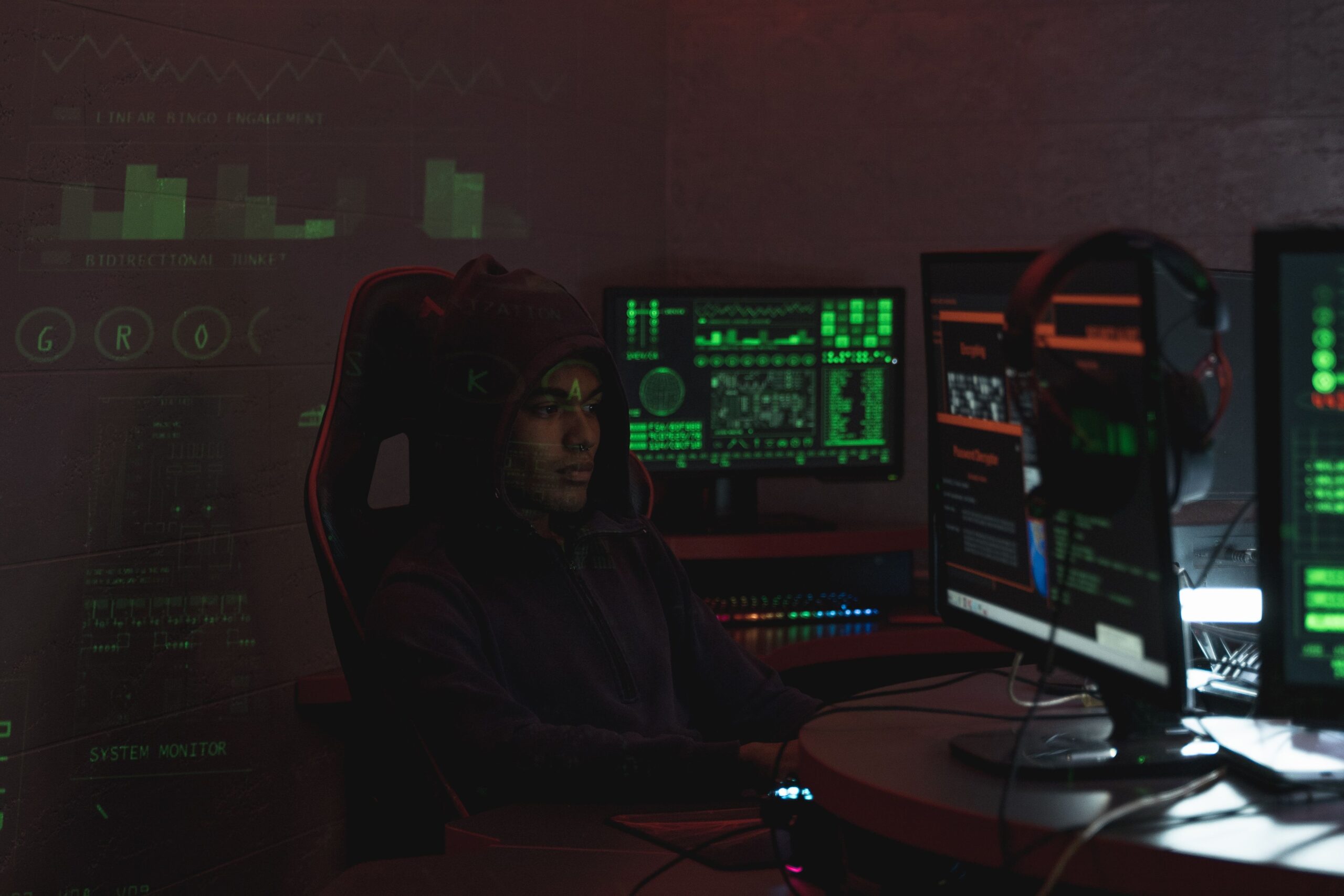 Hacker con capucha analizando datos en múltiples monitores en un entorno oscuro, ideal para introducir el concepto de robo de tokens en Discord.