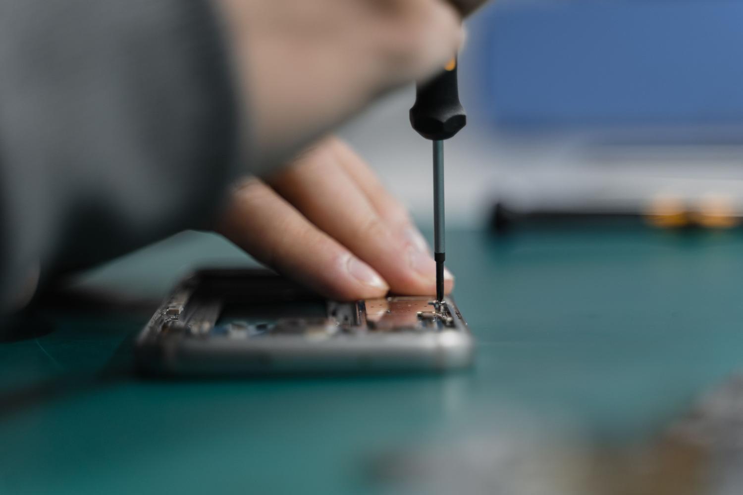 Primer plano de un técnico reparando un smartphone con herramientas de precisión sobre un tapete antiestático, ilustrando la auditoría técnica.