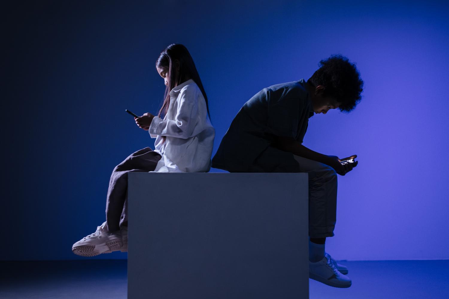 Siluetas de jóvenes utilizando smartphones bajo una iluminación azul intensa, evocando la conexión constante con la red.