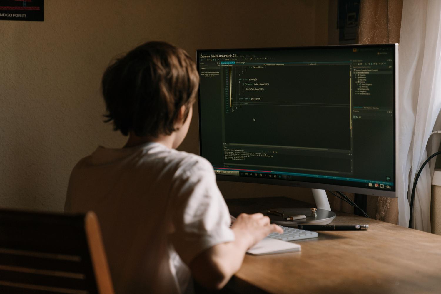 Joven programando software en un monitor de computadora en un entorno de oficina en casa