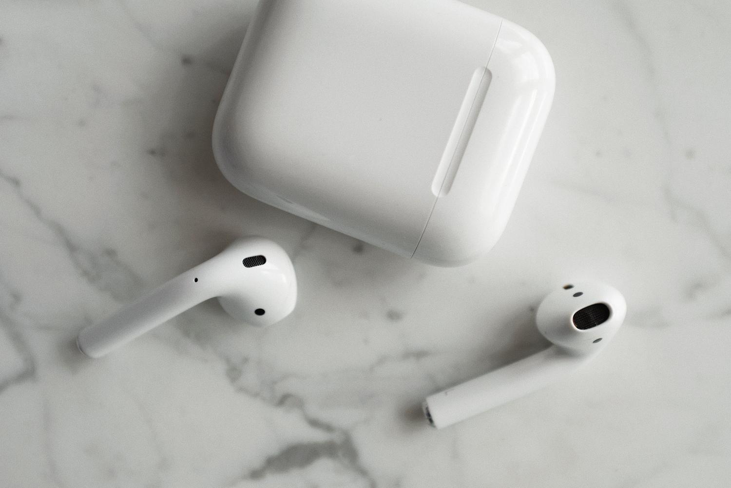 Primer plano de auriculares inalámbricos y su estuche de carga sobre una superficie de mármol.