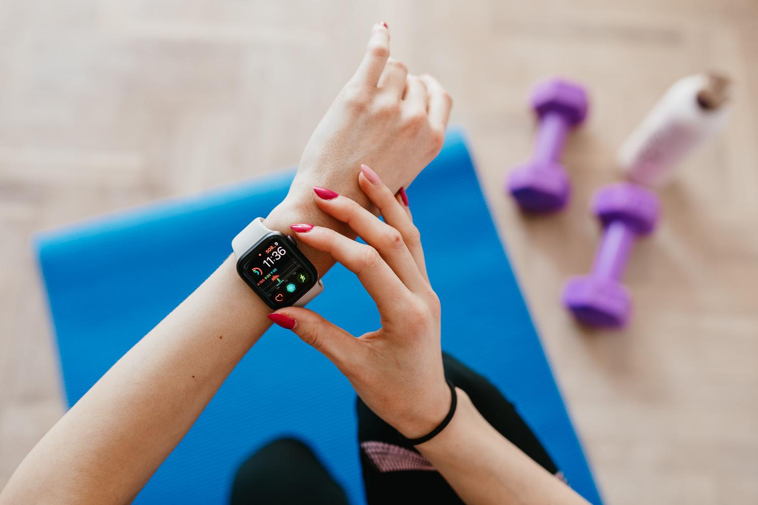 Mujer deportista revisando su reloj inteligente sobre una esterilla de yoga, representando el seguimiento de salud y fitness.