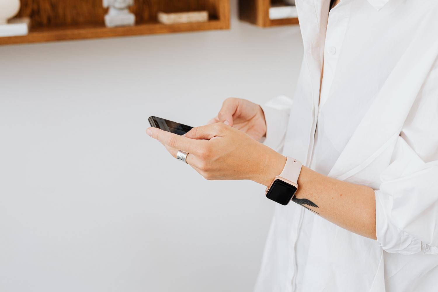 Persona utilizando un smartphone mientras lleva un reloj inteligente en la muñeca, ilustrando la conexión entre dispositivos.