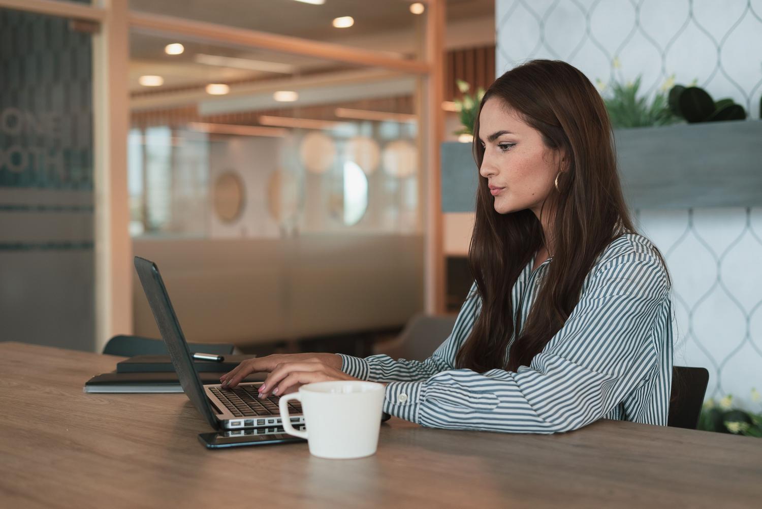 Mujer profesional trabajando con una computadora portátil en una oficina moderna, representando la interacción con el sistema operativo Windows.