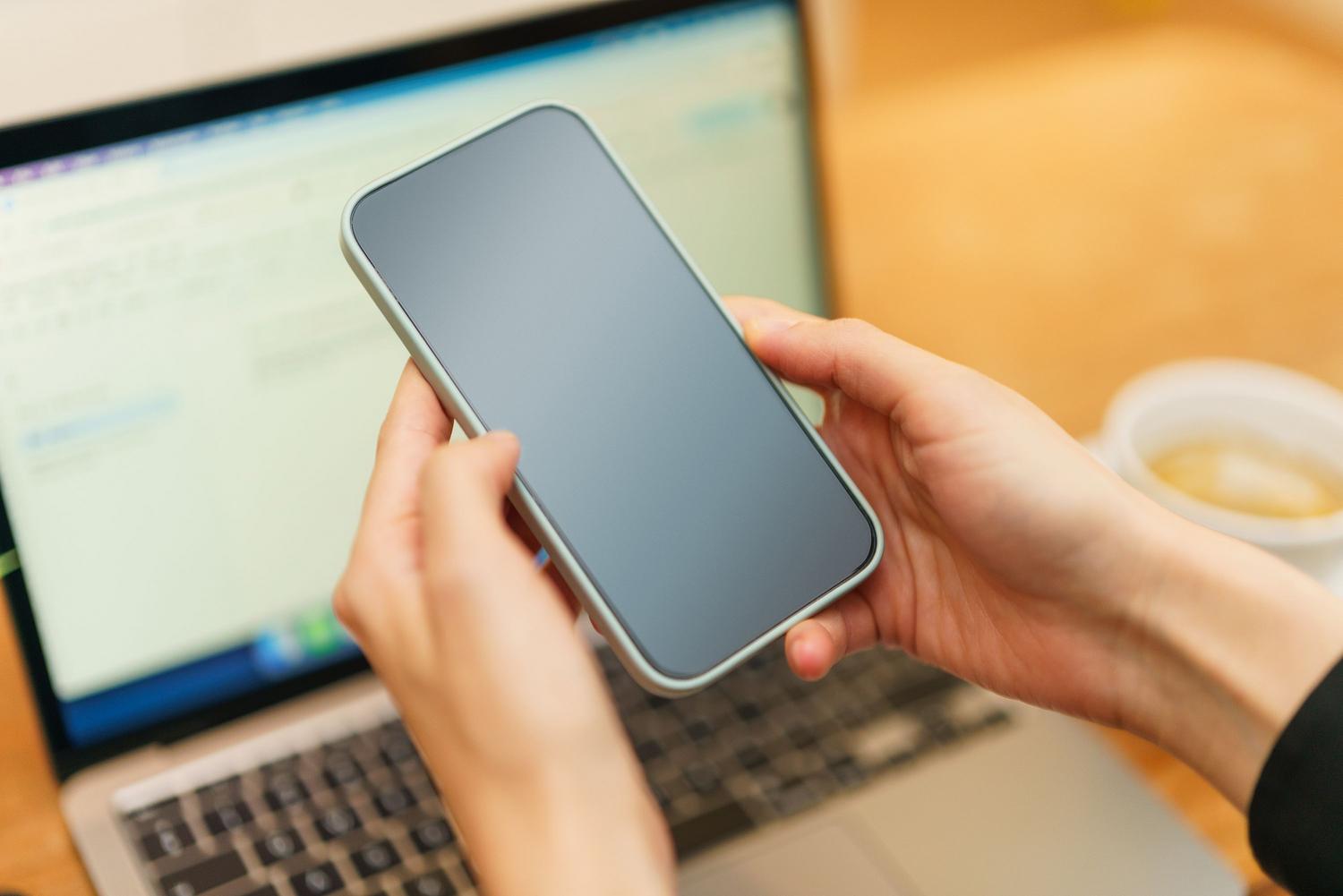 Persona sosteniendo un smartphone junto a un ordenador portátil y un café, ilustrando el uso de un punto de acceso portátil para el teletrabajo.