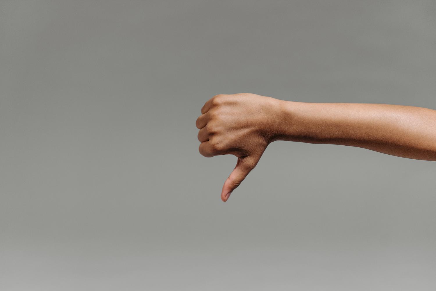 Primer plano de mano haciendo el gesto de pulgar abajo (Negativo) sobre fondo neutro para videollamadas de WhatsApp.