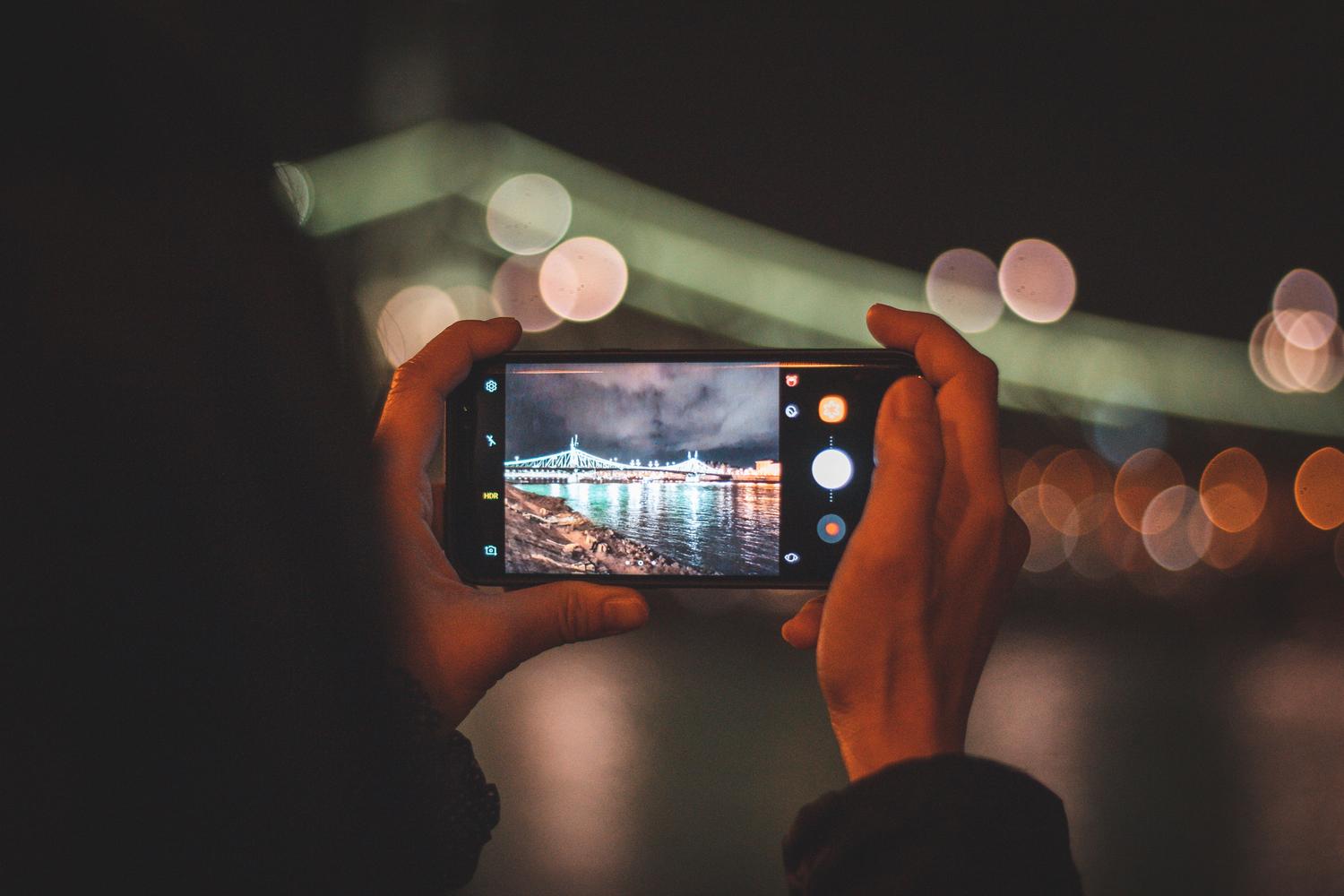 Primer plano de una persona capturando una vista nocturna de la ciudad con un smartphone, ilustrando la rapidez de captura.