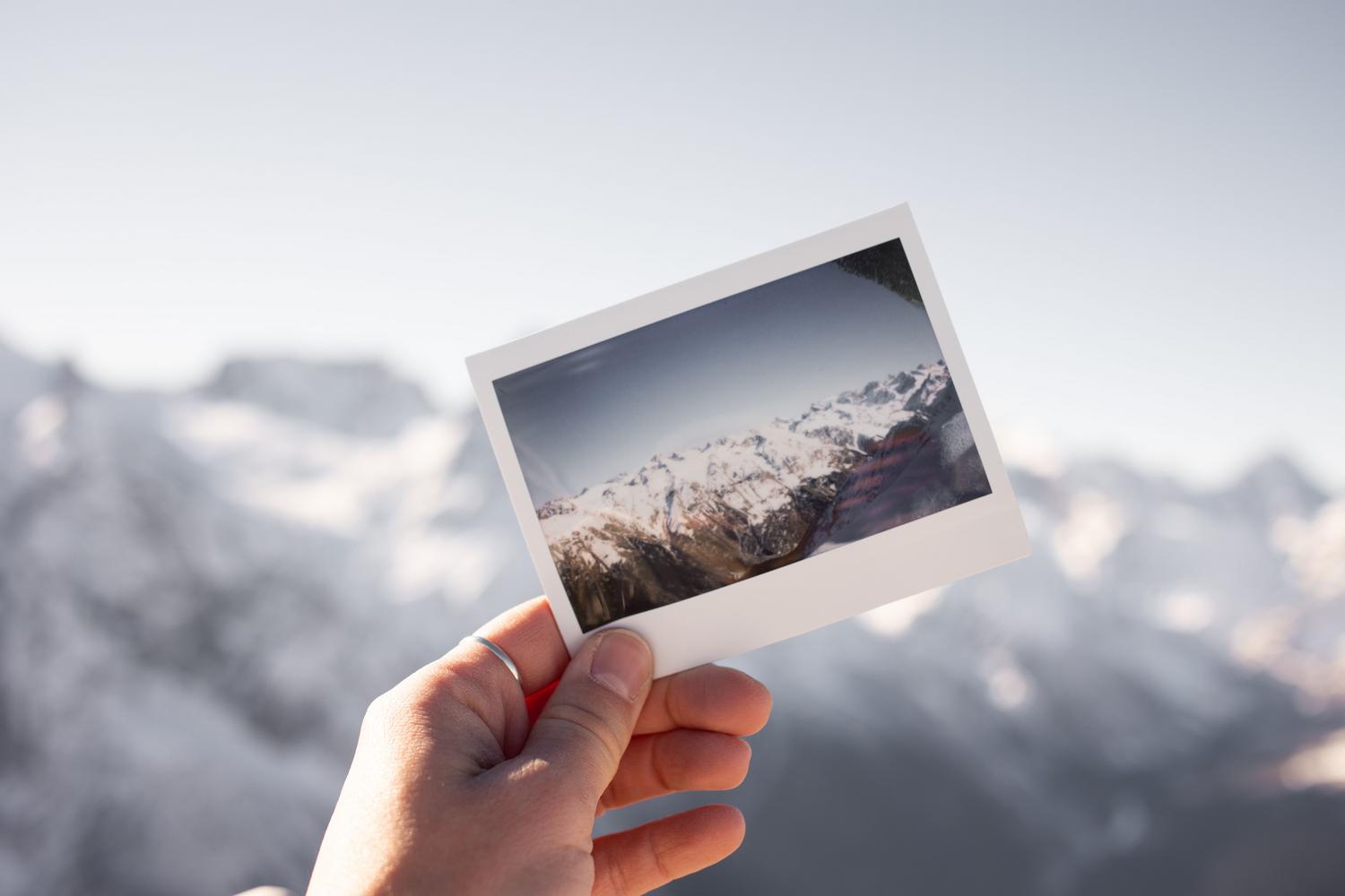 Una mano sostiene una fotografía instantánea estilo Polaroid de un paisaje montañoso, representando el efecto vintage de la IA.