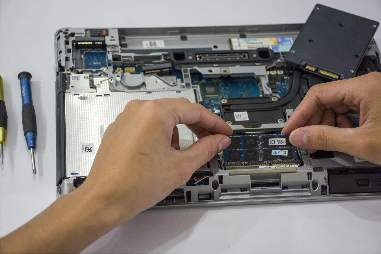 Technician installing a SODIMM RAM module into a laptop motherboard, illustrating the hardware upgrade process.