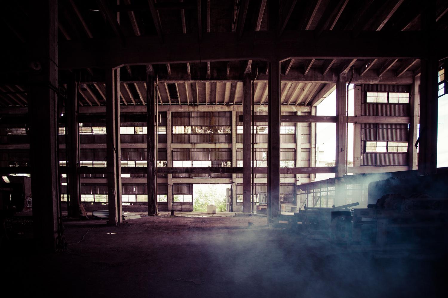 Interior de um almacén abandonado y polvoriento con estructuras metálicas oxidadas, representando los bunkers subterráneos y zonas de saqueo.