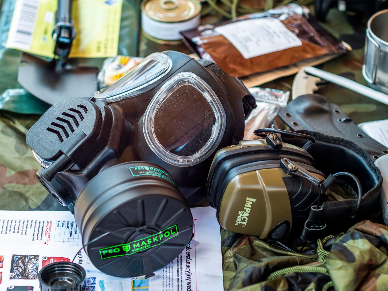 Equipo de supervivencia que incluye una máscara de gas y auriculares tácticos sobre un fondo camuflado, ilustrando el rol del scavenger o Vulture.