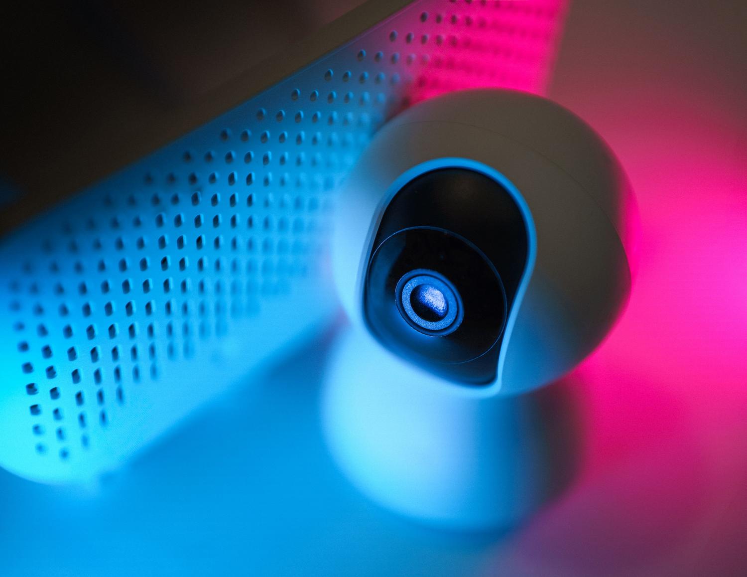 Cámara de seguridad moderna con iluminación neón azul y rosa, ilustrando la seguridad de dispositivos IoT y monitoreo físico.
