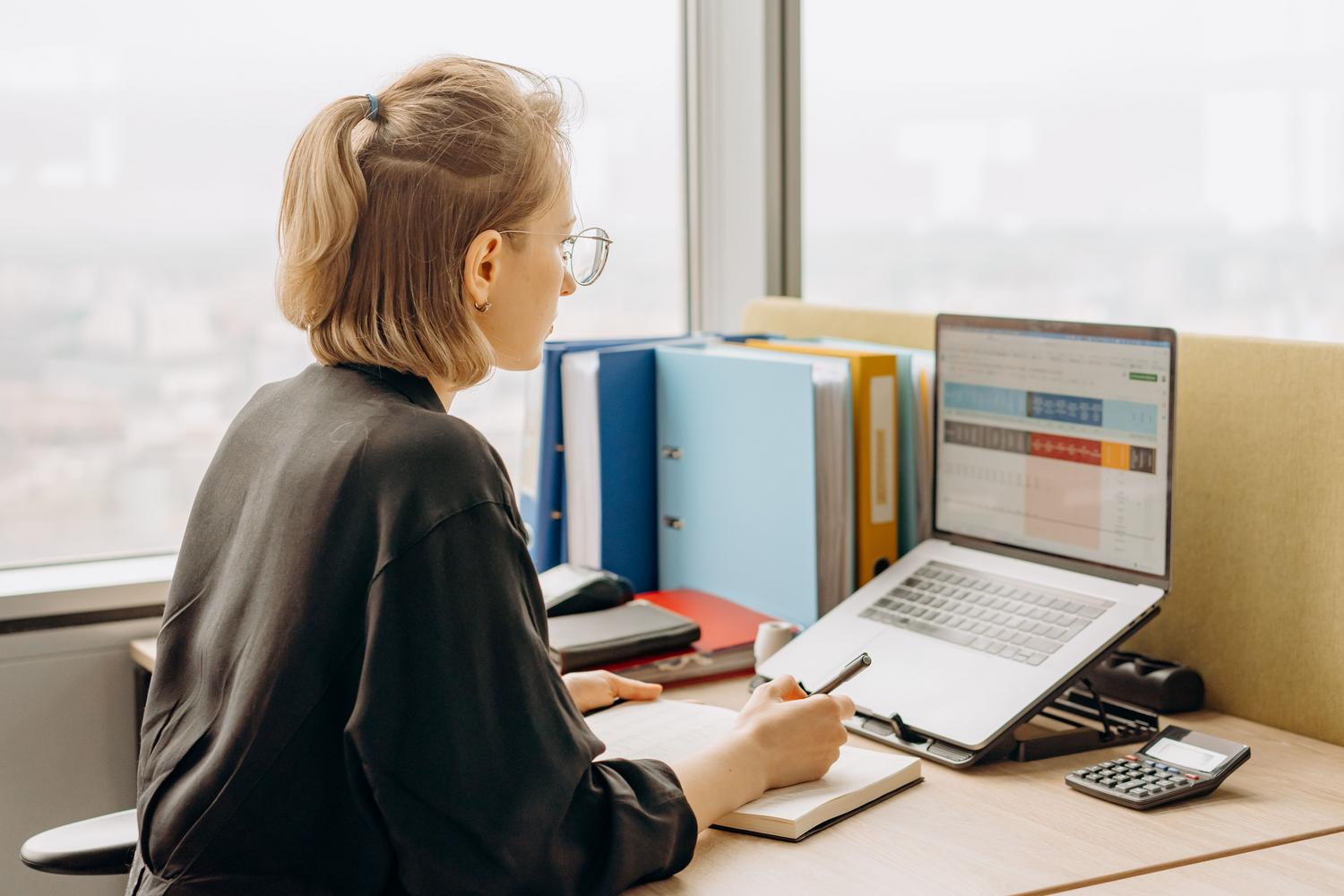 Mulher profissional trabalhando com planilhas em um notebook em um escritório moderno.