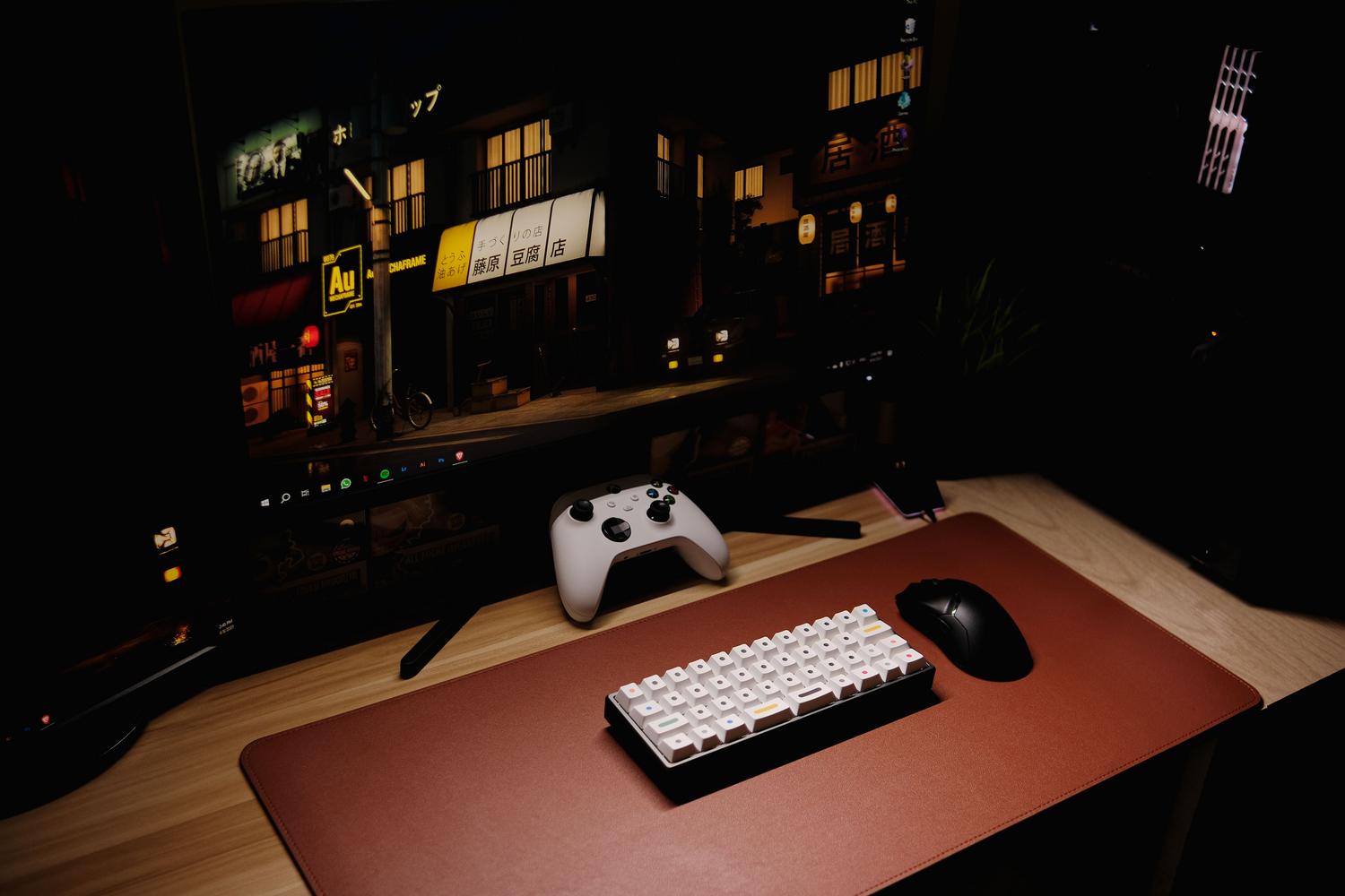 Setup gaming nocturno com monitor ultrawide e teclado mecánico compacto sobre um tapete de cuero.