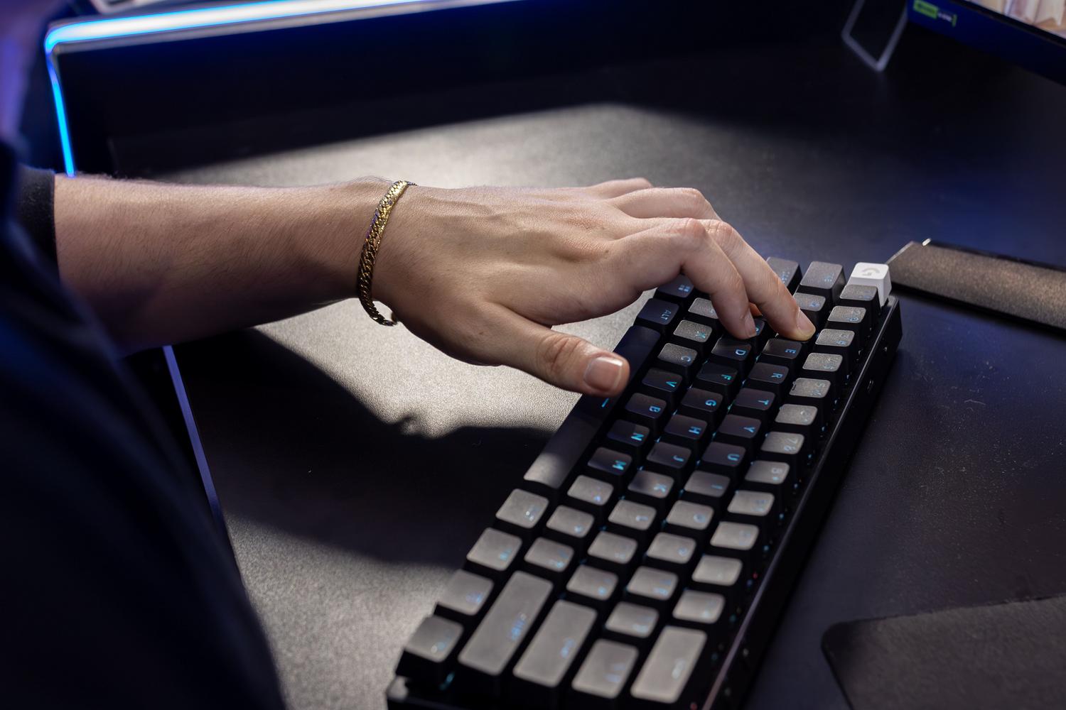 Primer plano de una persona escribiendo en un teclado mecánico retroiluminado en color azul, ideal para entornos de trabajo y gaming modernos.