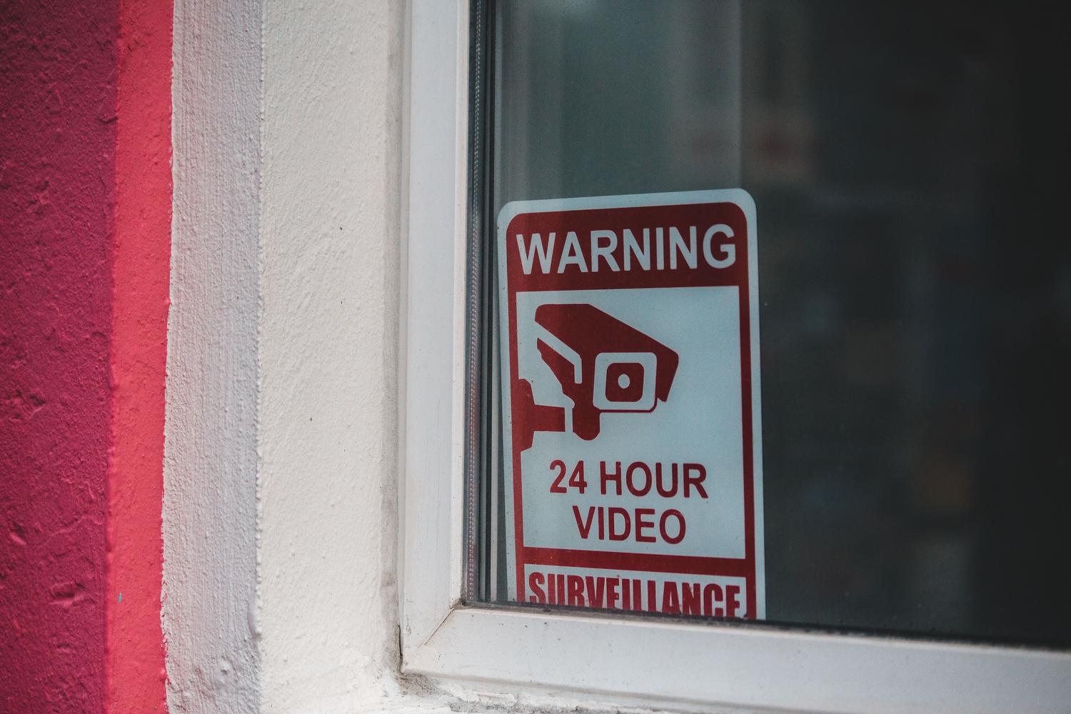 Cartel informativo de advertencia de videovigilancia 24 horas colocado en el cristal de una ventana.