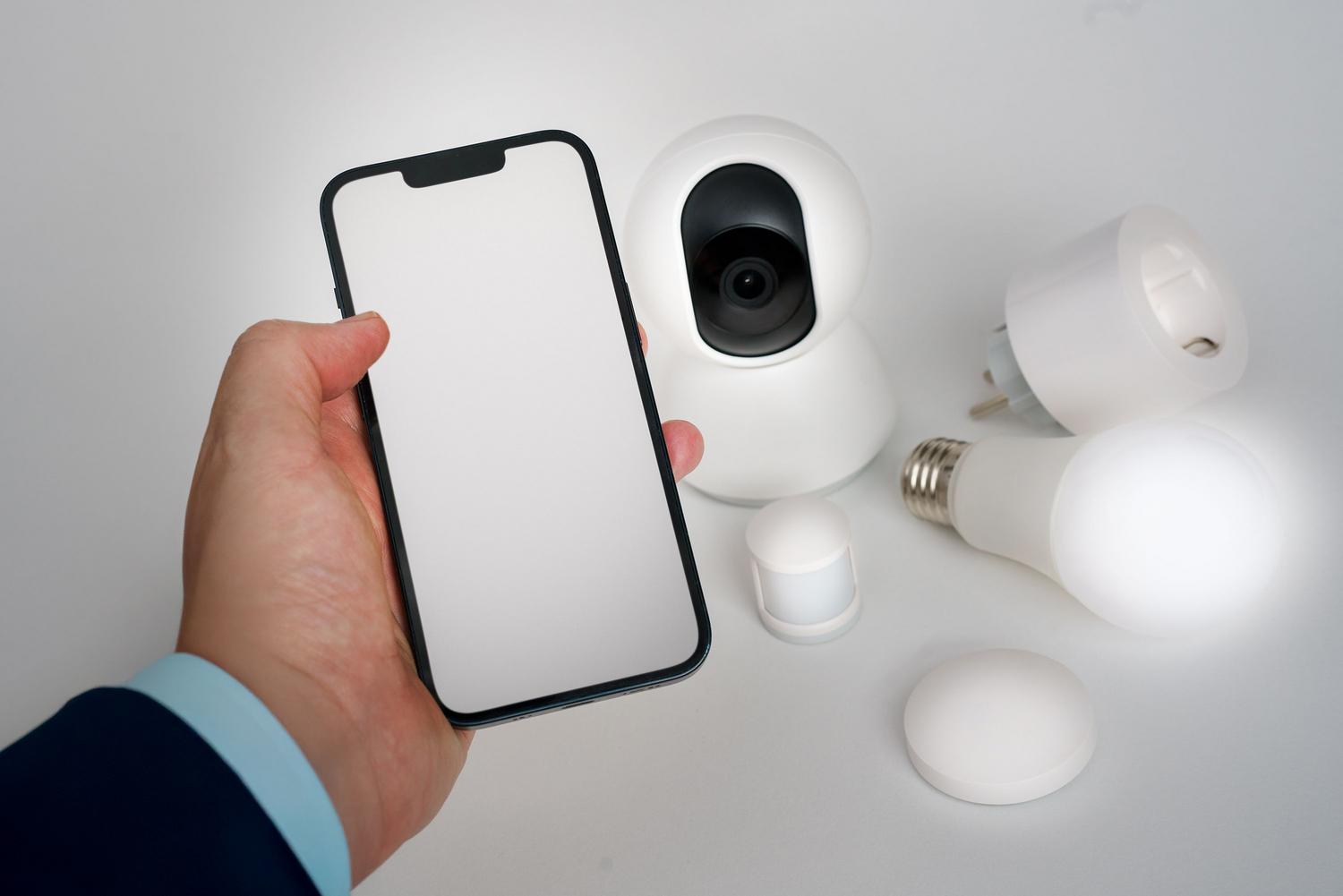 Persona controlando diversos dispositivos del hogar inteligente desde un smartphone, incluyendo cámara de seguridad y bombilla LED.