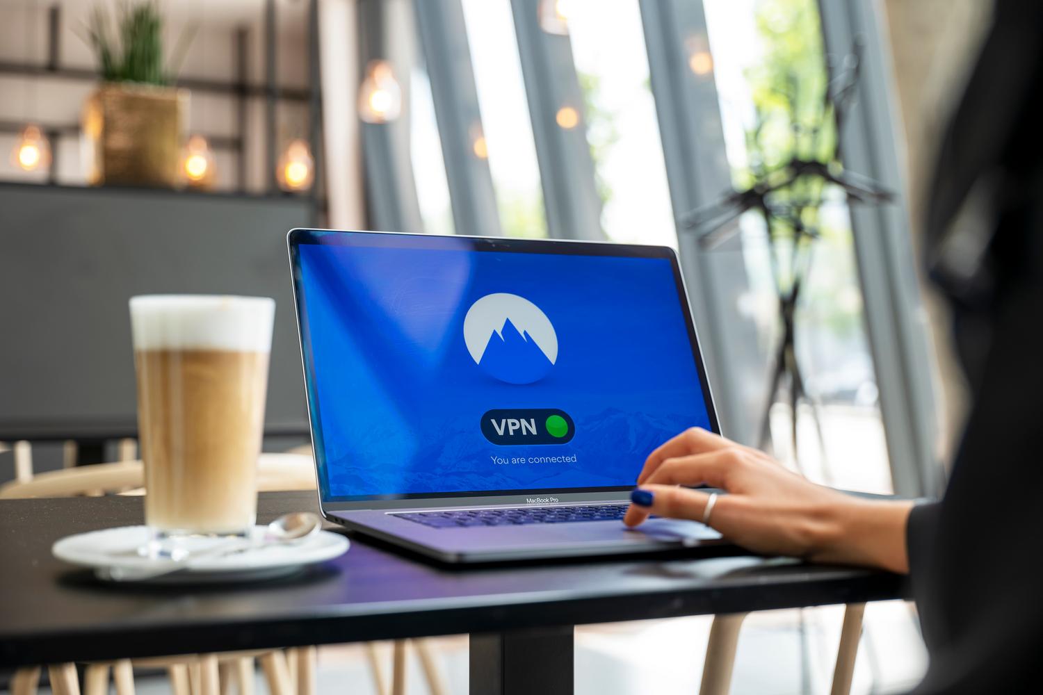 Persona utilizando un portátil con conexión VPN en una cafetería moderna, ilustrando el uso seguro de redes Wi-Fi públicas.
