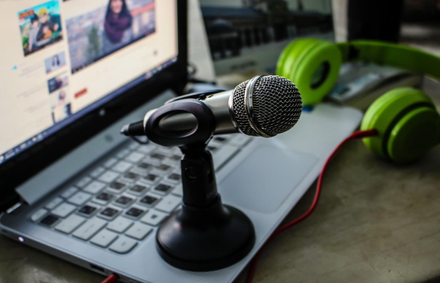Set de grabación con micrófono, ordenador portátil y auriculares verdes, evocando un ambiente de podcasting o teletrabajo.