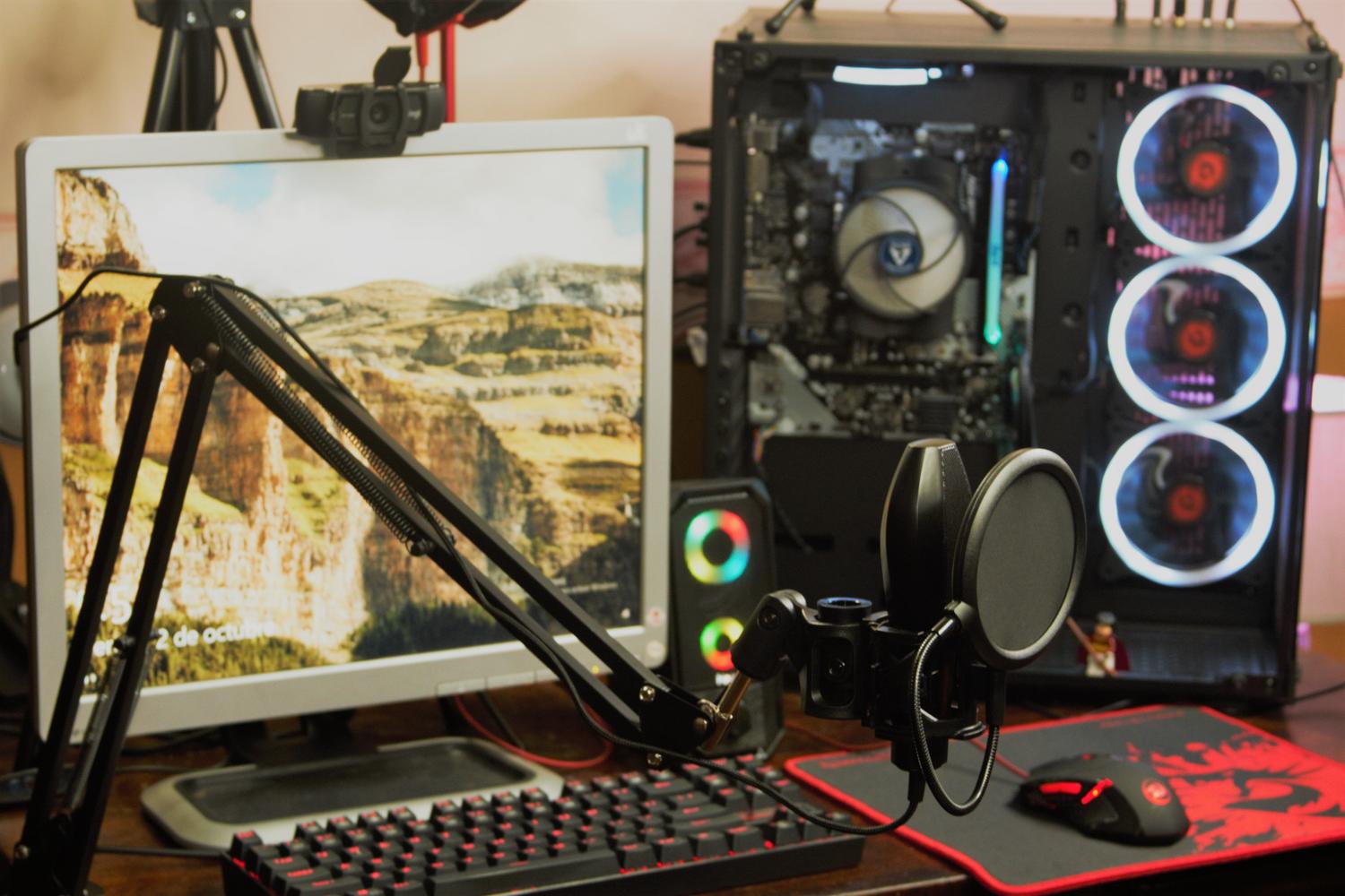 Configuración de ordenador moderna con micrófono profesional, monitor y torre PC con iluminación RGB, representando un entorno de trabajo actual.