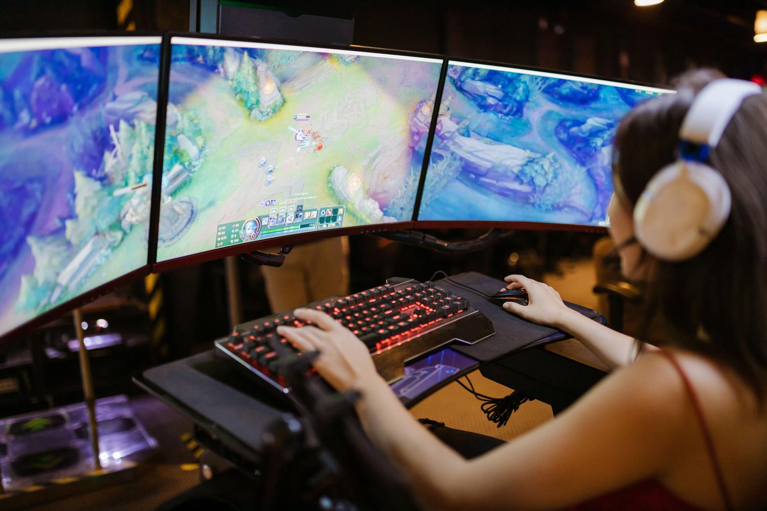 Gamer concentrada con configuración de triple monitor, ilustrando la inmersión total al jugar títulos de alta calidad.