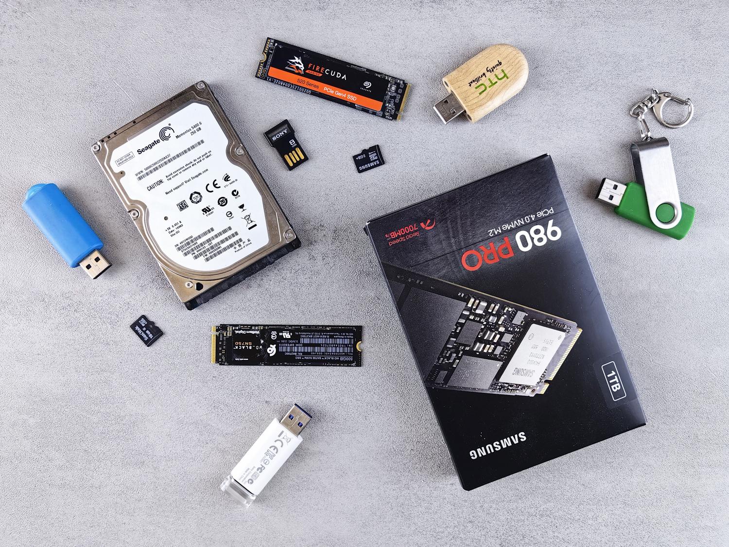 Vista cenital de diversos dispositivos de almacenamiento incluyendo HDDs, SSDs NVMe, memorias USB y tarjetas SD. Vista cenital de diversos dispositivos de almacenamiento incluyendo HDDs, SSDs NVMe, memorias USB y tarjetas SD.