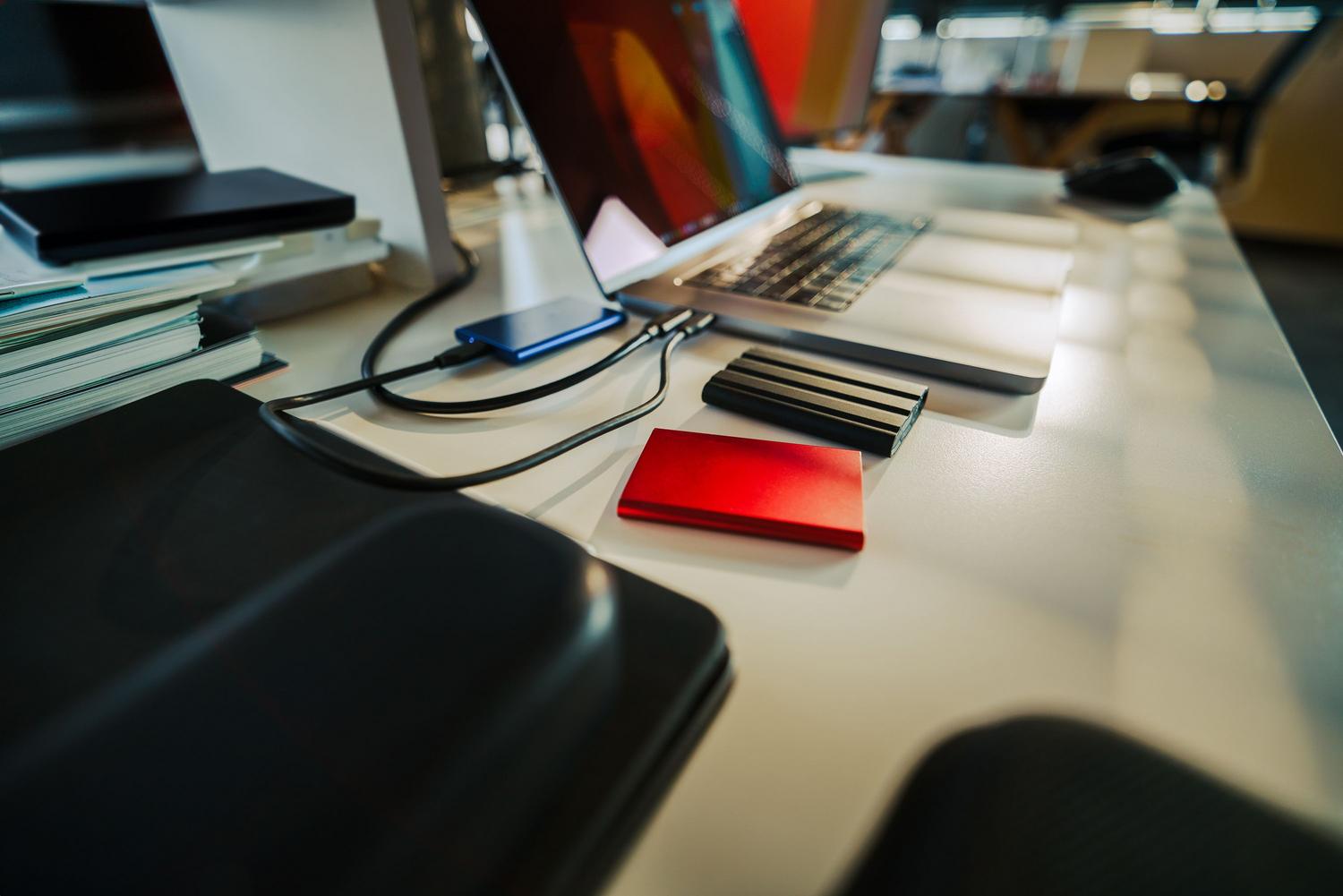 Espacio de trabajo moderno con un ordenador portátil y varios discos duros externos para almacenamiento de datos.