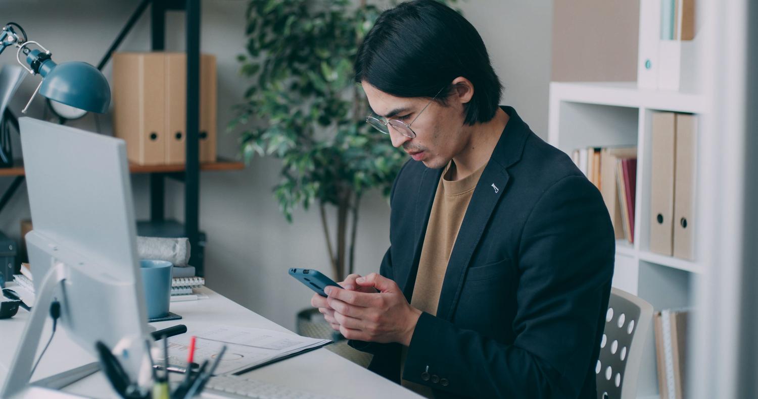 Joven profesional en una oficina moderna utilizando su smartphone mientras trabaja, ilustrando los trucos de productividad de MIUI.