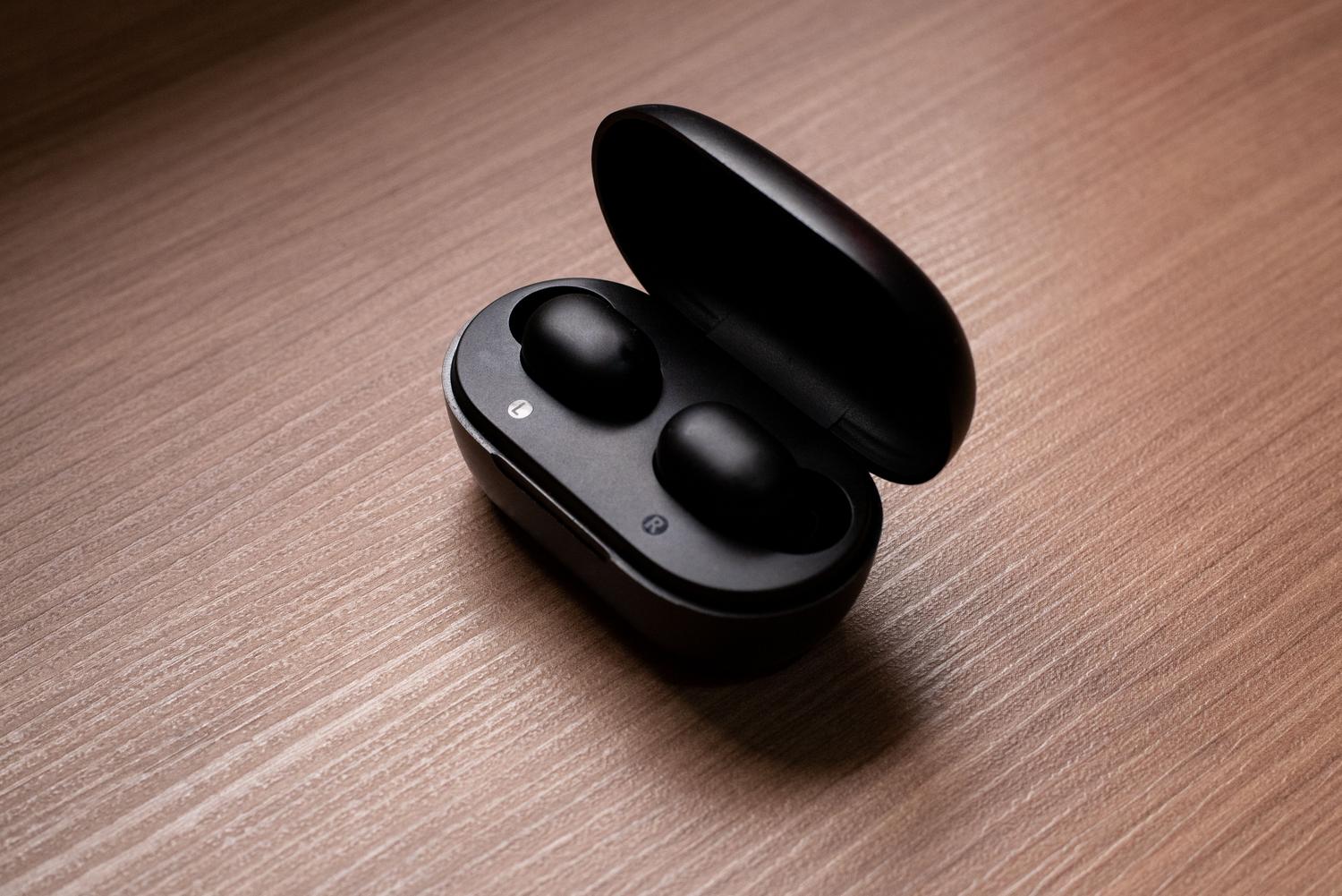 Auriculares inalámbricos negros en su estuche de carga abierto sobre una mesa de madera