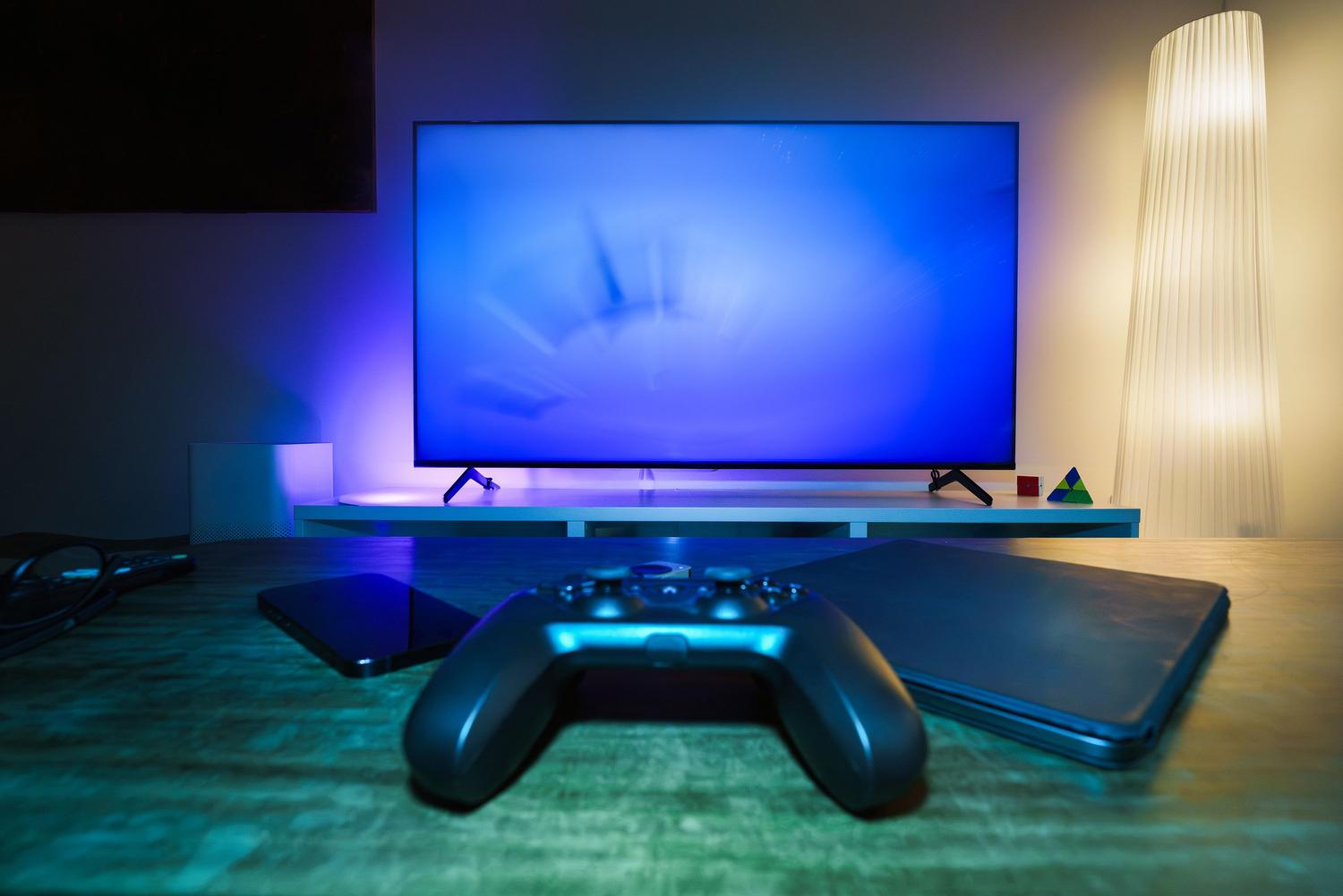 Configuración de juego moderna y elegante con mando, dispositivos inteligentes y televisor en una sala de estar iluminada.