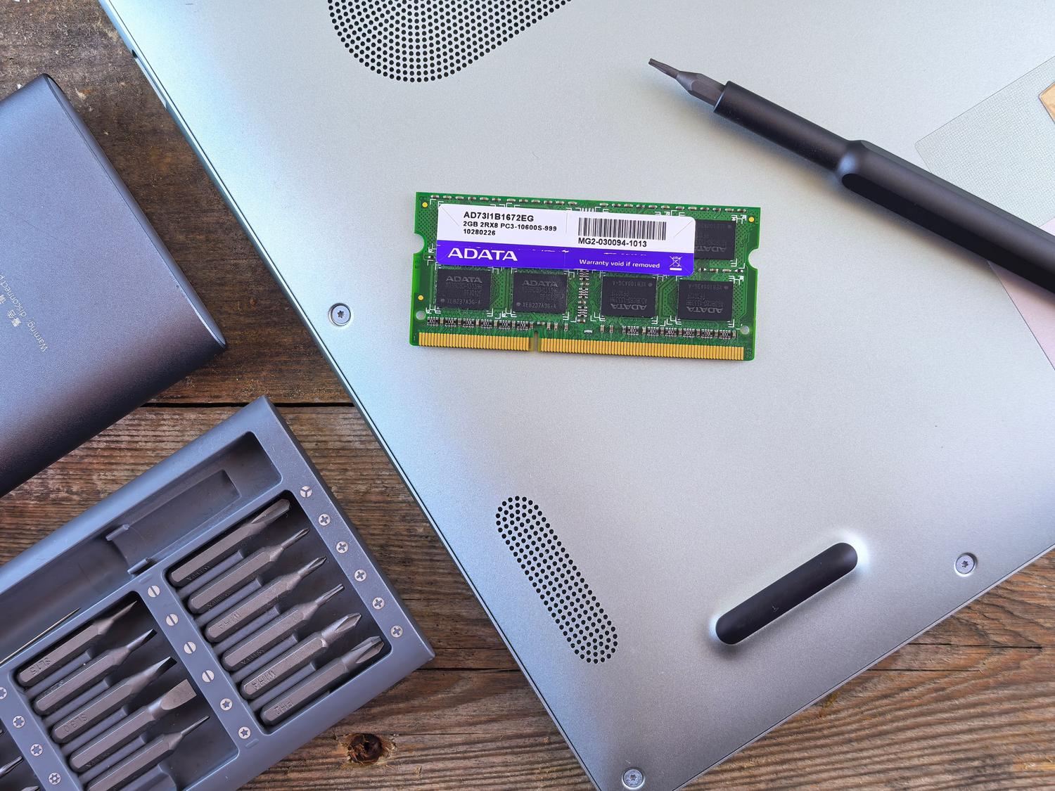 Herramientas de reparación y un módulo de memoria RAM junto a un portátil abierto, ilustrando el proceso de actualización de hardware.